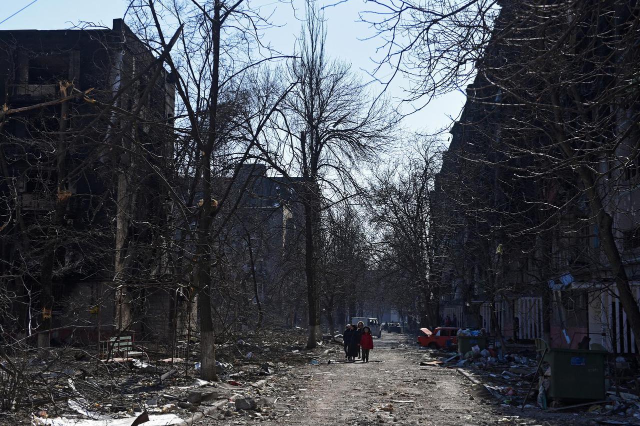 Local residents walk near damaged residential buildings in the besieged city of Mariupol