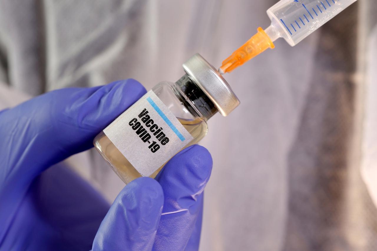 FILE PHOTO: A woman holds a small bottle labeled with a "Vaccine COVID-19" sticker and a medical syringe in this illustration