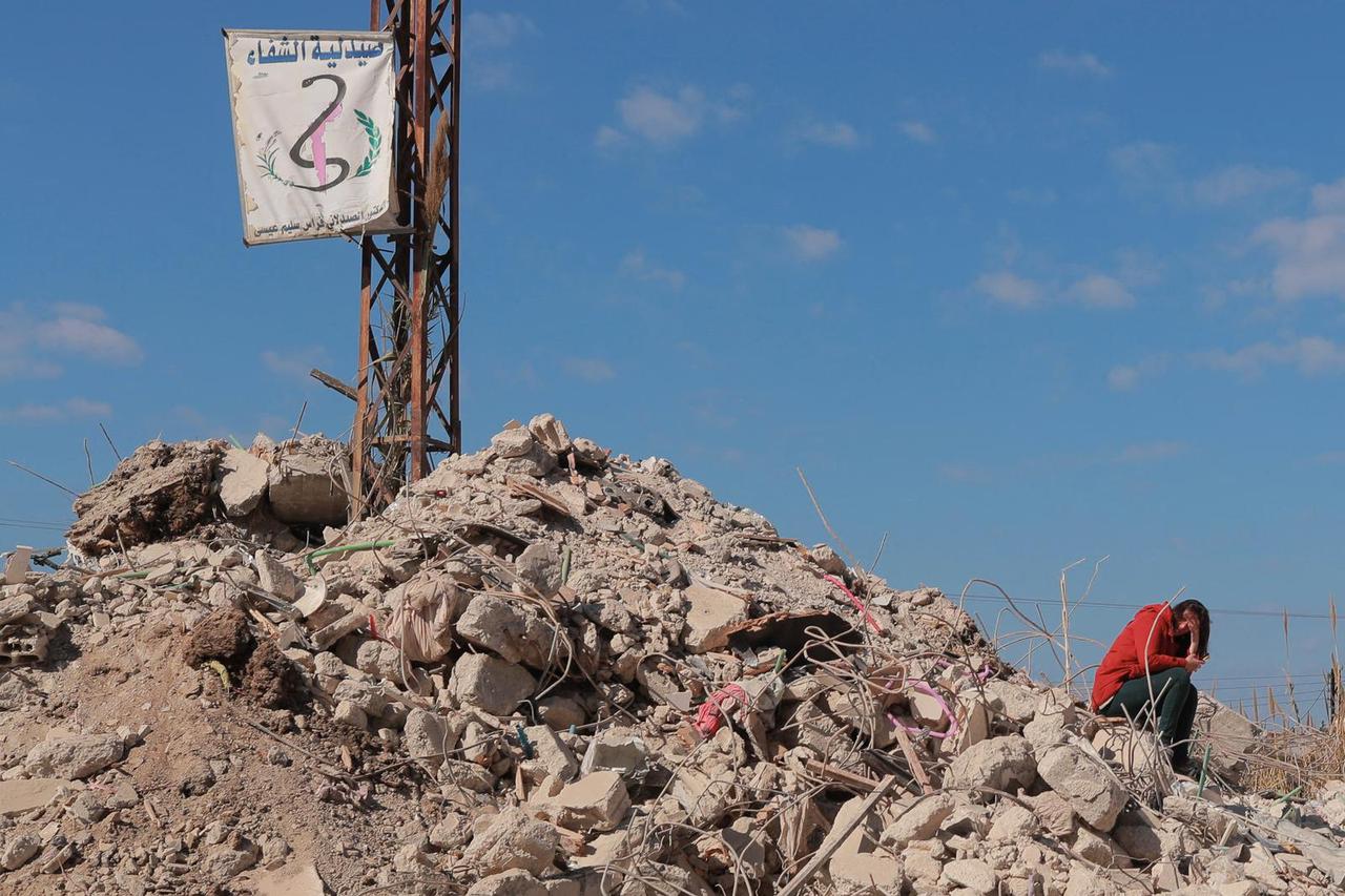 A woman sits on the rubble of her destroyed home in Jableh