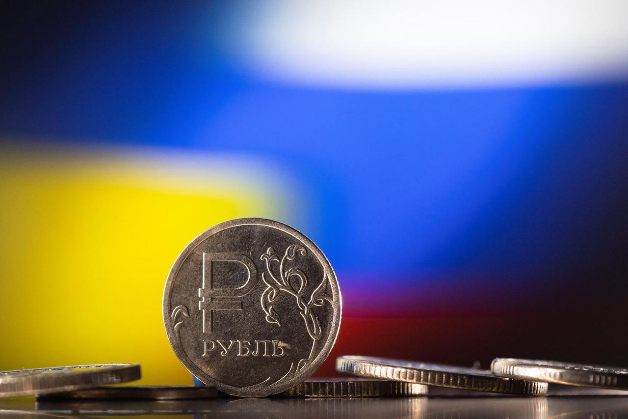 Illustration shows Russian Rouble coins are seen in front of displayed Ukrainian's and Russia's flag colours