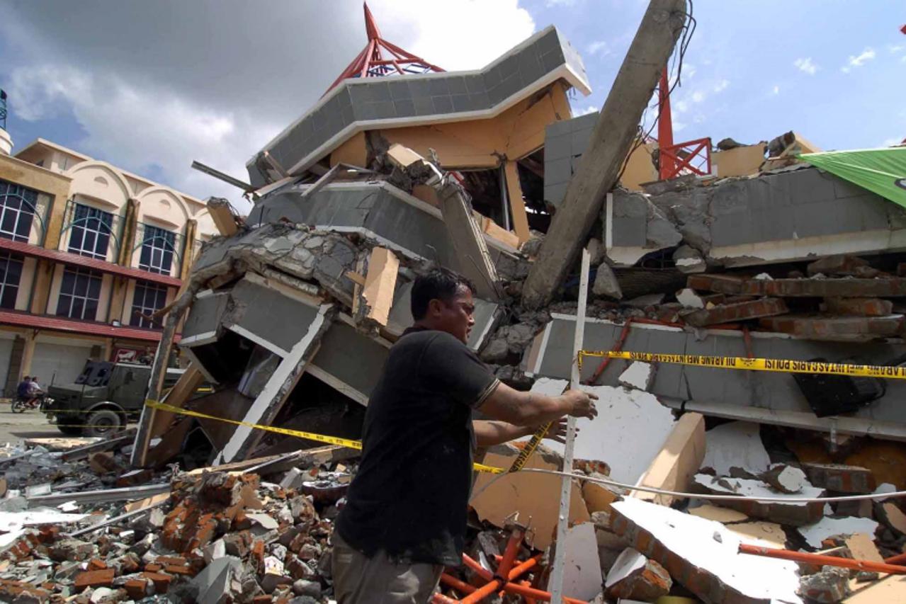 'A plainclothes policeman secures the area around a destroyed building in Banda Aceh, 27 December 2004 after a devastating quake and series of tidal waves struck the province. Indonesia\'s remote Aceh