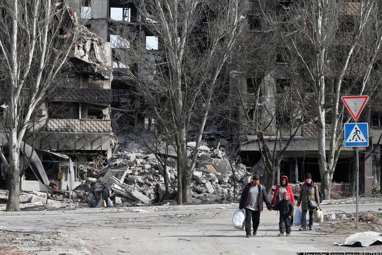 Local residents walk past a destroyed apartment building in Mariupol