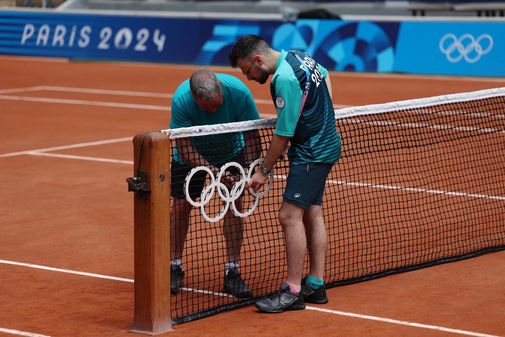 Paris 2024 Olympics - Tennis - Practice - Roland-Garros, Paris, France - July 22, 2024. Ground workers attach Olympic rings to the net ahead of practice REUTERS/Claudia Greco Photo: CLAUDIA GRECO/REUTERS