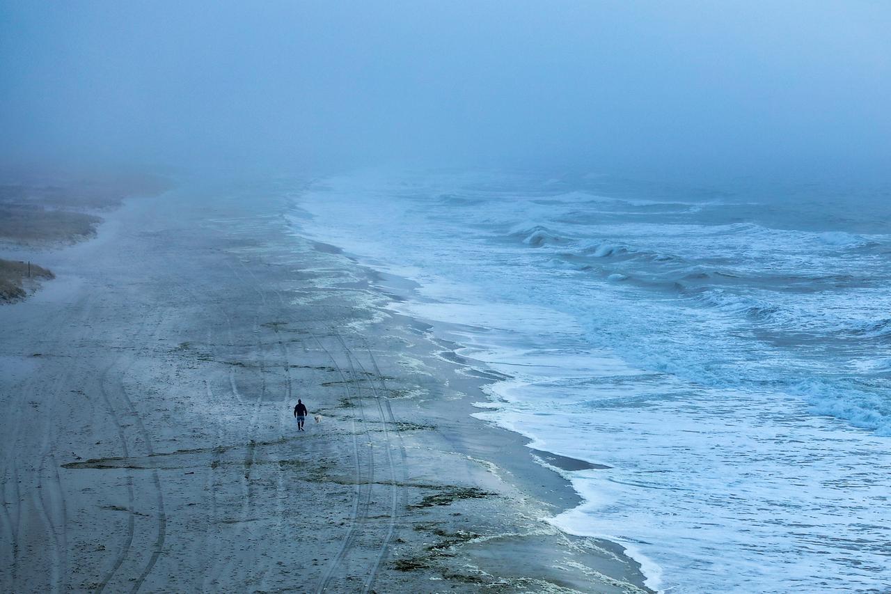 A drone view shows a man and a dog walking along the Atlantic Ocean on Lido Beach in Hempstead, New York