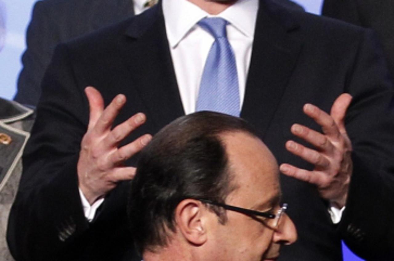 'British Prime Minister David Cameron gestures as French President Francois Hollande walks past during a family picture of NATO leaders at the NATO Summit in Chicago, May 21, 2012.  REUTERS/Andrew Win