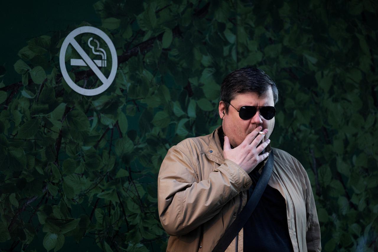 A man smokes a cigarette as he stands near a “No smoking” sign in the street in Moscow