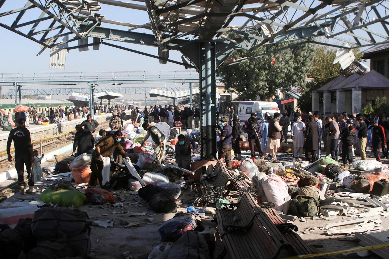 Police officers and people gather at the site amid the debris after a bomb blast at a railway station in Quetta