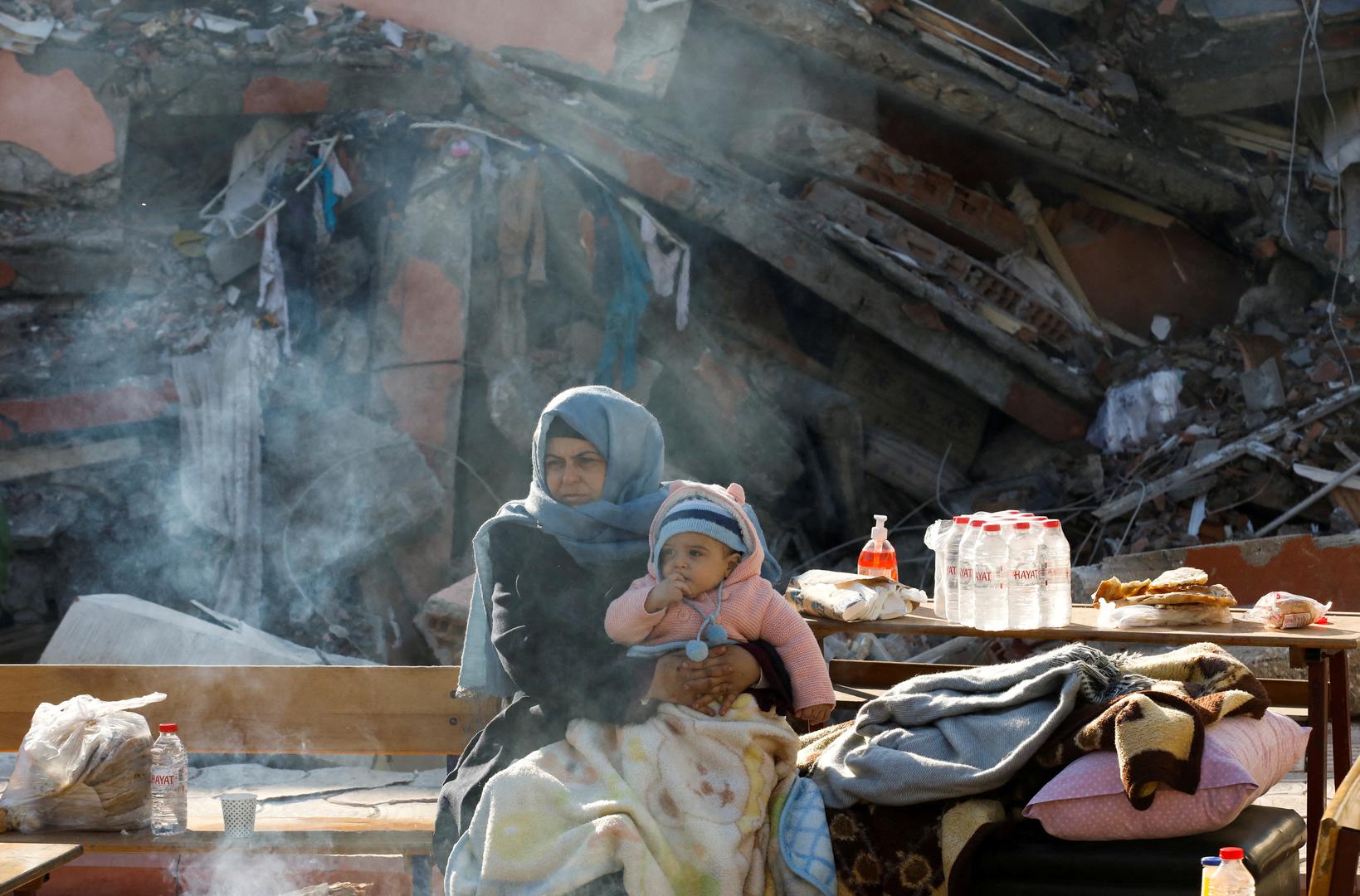 A woman holding a child sits by a collapsed building as search for survivors continues, in the aftermath of a deadly earthquake in Hatay, Turkey, February 10, 2023. REUTERS/Umit Bektas       TPX IMAGES OF THE DAY Photo: UMIT BEKTAS/REUTERS