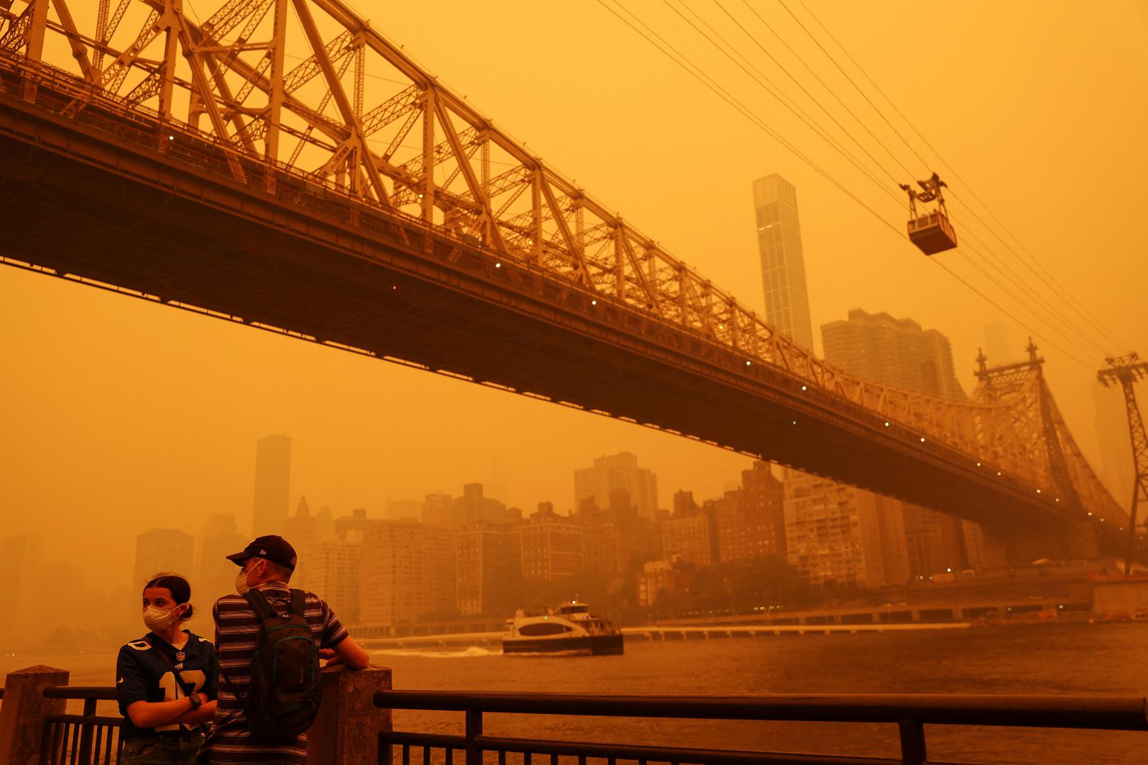 People wear protective masks as the Roosevelt Island Tram crosses the East River while haze and smoke from the Canadian wildfires shroud the Manhattan skyline in the Queens Borough New York City, U.S., June 7, 2023. REUTERS/Shannon Stapleton Photo: SHANNON STAPLETON/REUTERS