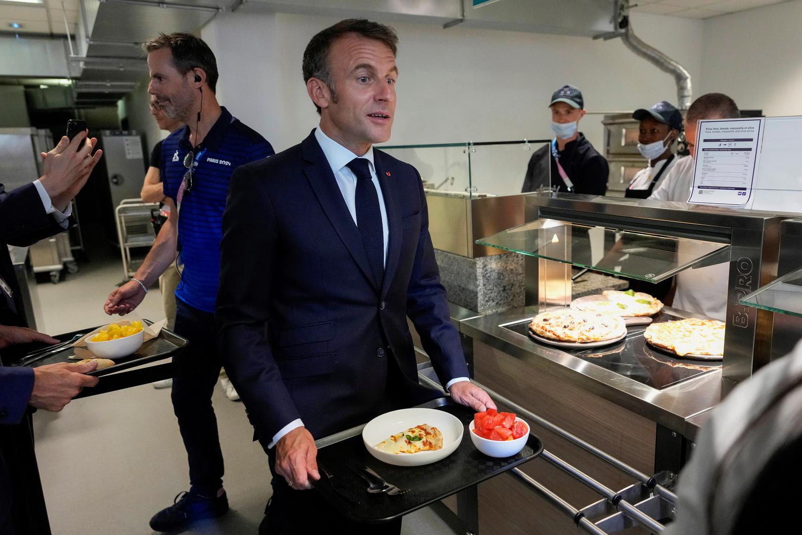 French President Emmanuel Macron holds his plate as he visits the Olympic village for the 2024 Summer Olympics, in Paris, France, July 22, 2024.     Michel Euler/Pool via REUTERS Photo: MICHEL EULER/REUTERS