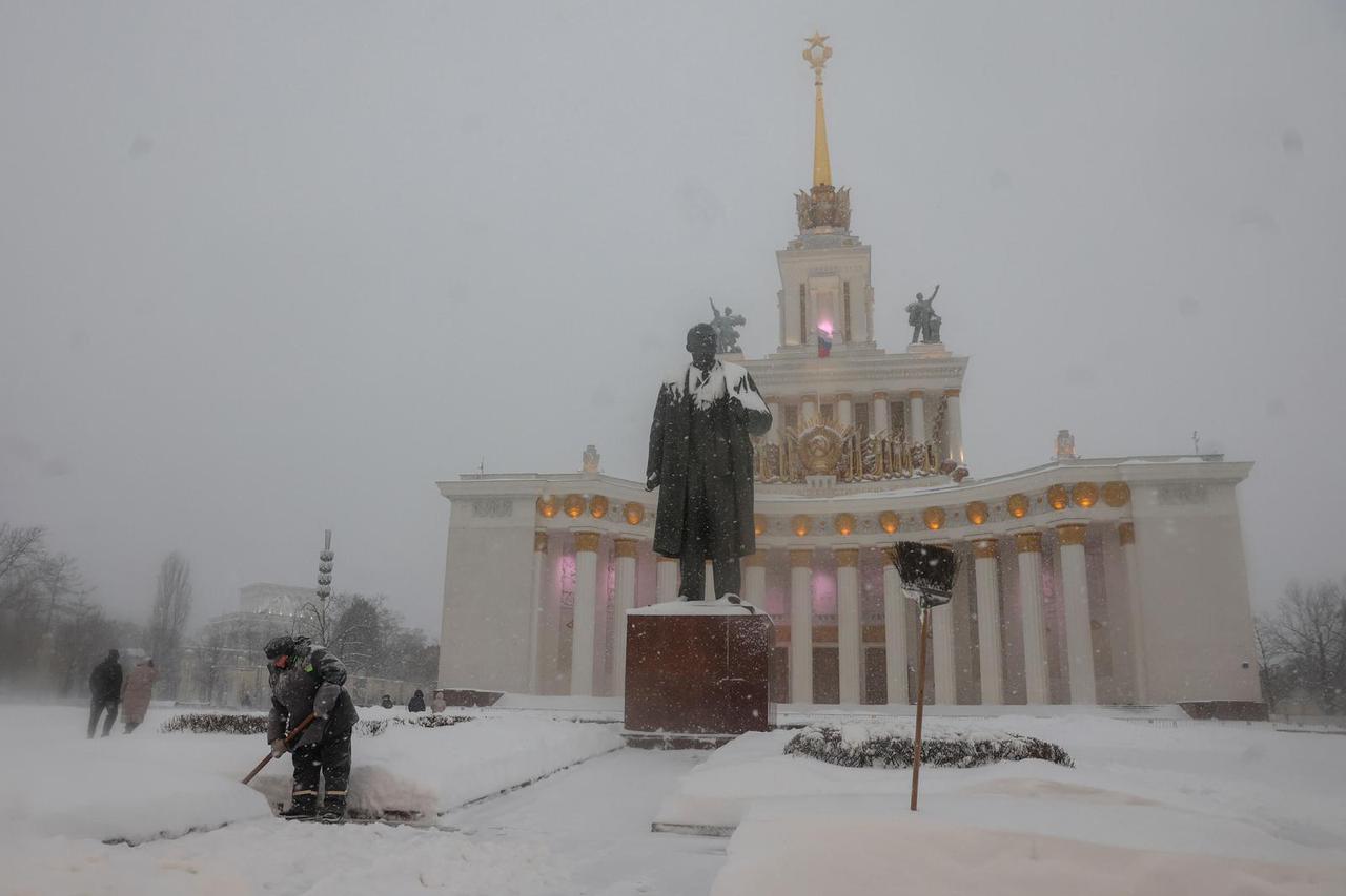 A worker cleans snow next to the statue of Soviet state founder Vladimir Lenin during snowfall at the Exhibition of Achievements of National Economy (VDNKh) in Moscow