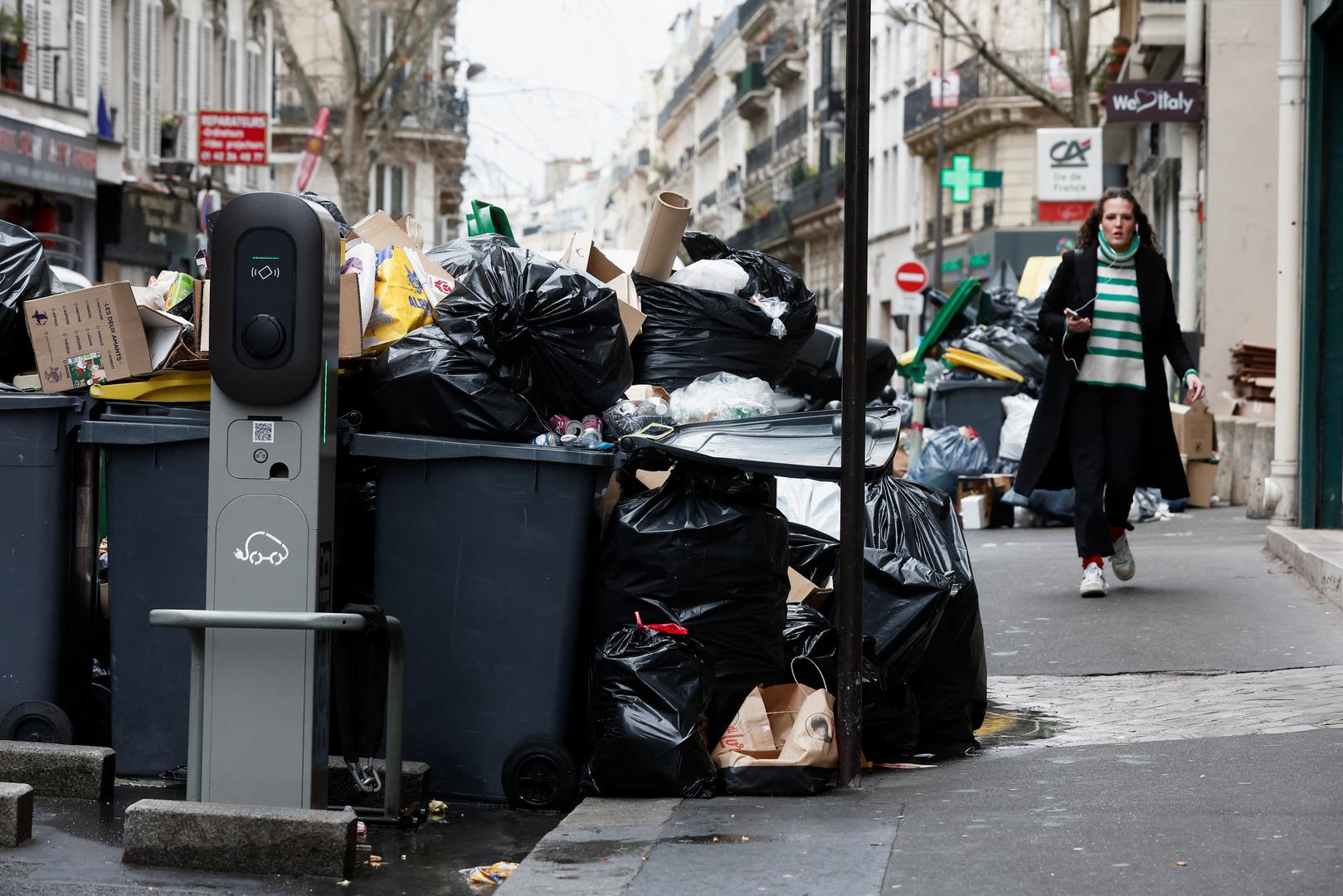 People walk in a street where garbage cans are overflowing, as garbage has not been collected, in Paris, France March 13, 2023. REUTERS/Benoit Tessier Photo: BENOIT TESSIER/REUTERS