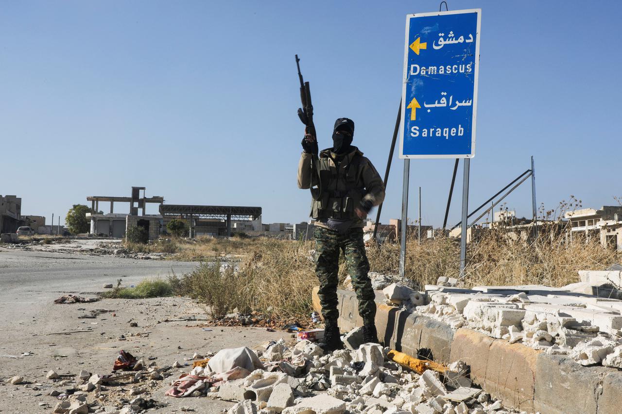 A rebel fighter carries a weapon as he stands at the entrance of Saraqeb town