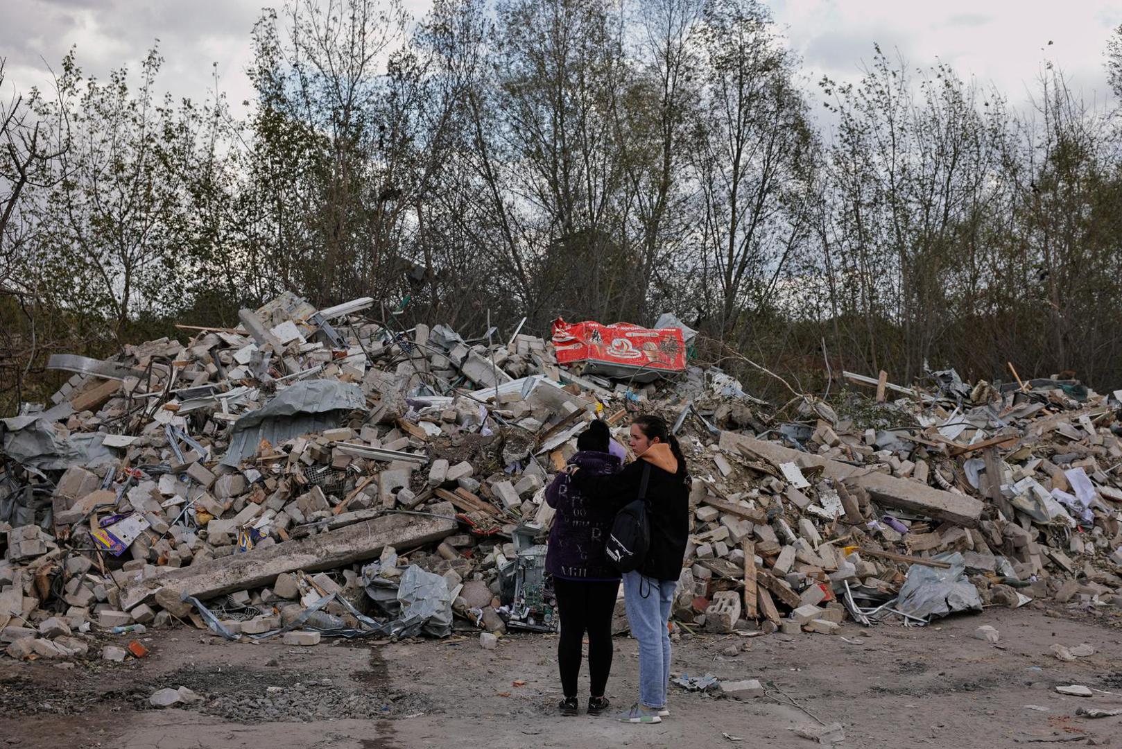 Two women react in front of a pile of rubble that is left of the cafe that hosted the wake and was hit by a Russian missile, following a Russian military strike, amid Russia's attack on Ukraine, in the village of Hroza, Kharkiv region, Ukraine October 6, 2023. REUTERS/Thomas Peter Photo: Thomas Peter/REUTERS