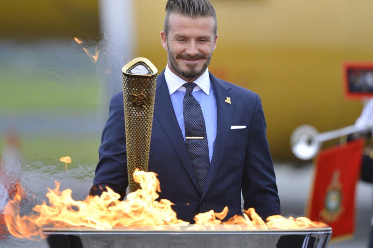 'British soccer player and London 2012 Olympic Games ambassador David Beckham reacts after lighting the Olympic torch with a cauldron after arriving at RNAS Culdrose base near Helston in Cornwall, sou