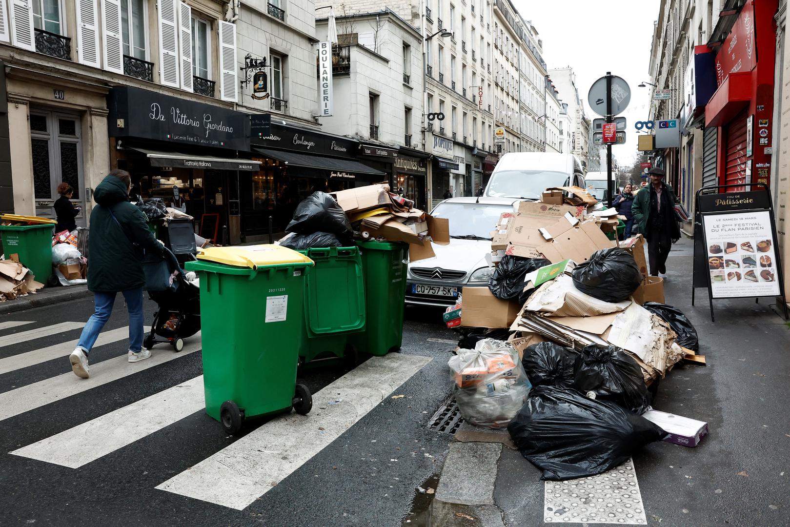 People walk in a street where garbage cans are overflowing, as garbage has not been collected, in Paris, France March 13, 2023. REUTERS/Benoit Tessier Photo: BENOIT TESSIER/REUTERS